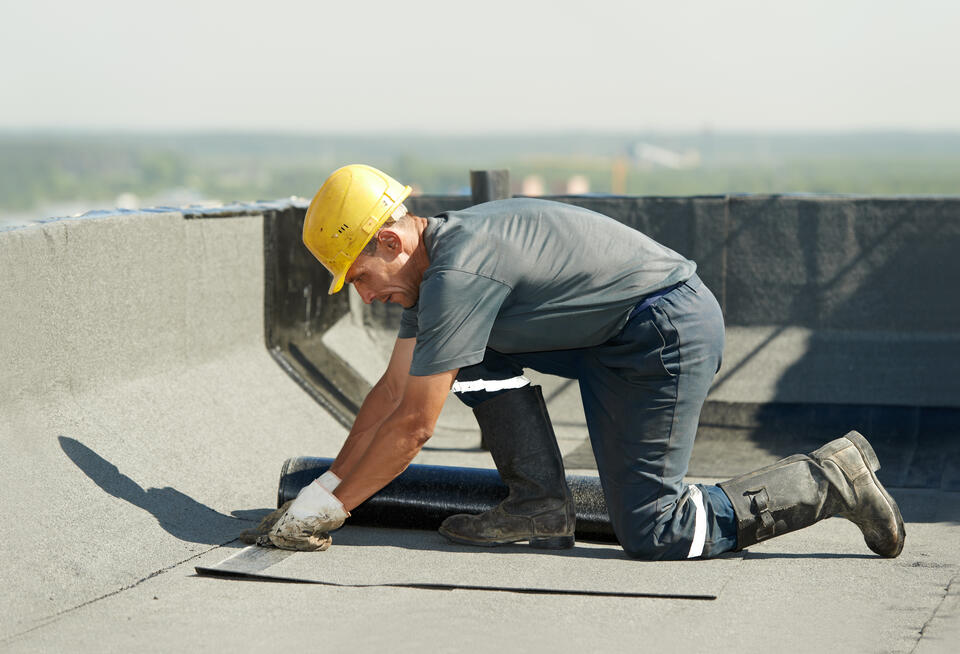 commercial roof leak repair-roofer in hard hat repairing a section of commercial flat roof